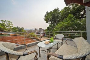 A balcony with wicker furniture, a table, and a view of a construction site. - HashTag Villa 2BHK in Lonavala (Kune N.m.)