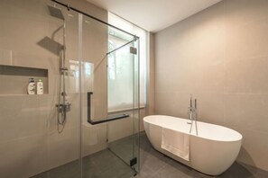 A modern bathroom with a glass-enclosed shower, a freestanding bathtub, and a shelf with toiletries. - Long One A5 (Phuket)