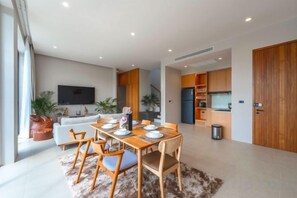 A modern living room with a dining area, a kitchen, and a TV mounted on the wall. - Long One A5 (Phuket)