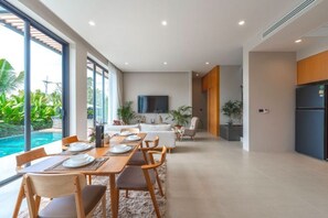 A modern dining area with a long table, chairs, and a view of a swimming pool. - Long One A5 (Phuket)