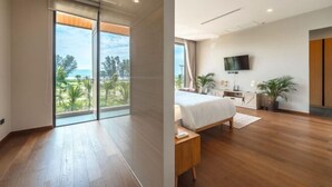 A modern bedroom with a large bed, a TV, and a balcony with a view of greenery. - Long One A5 (Phuket)