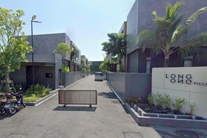 A residential street with modern buildings, a gated entrance, and a clear sky. - Long One A5 (Phuket)