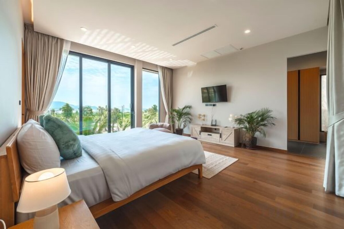 A modern bedroom with a large bed, a flat-screen TV, and a view of the outdoors.
