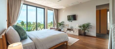 A modern bedroom with a large bed, a flat-screen TV, and a view of the outdoors.