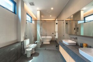 A modern bathroom with a bathtub, two toilets, a large mirror, and a countertop with a sink. - Long One A5 (Phuket)