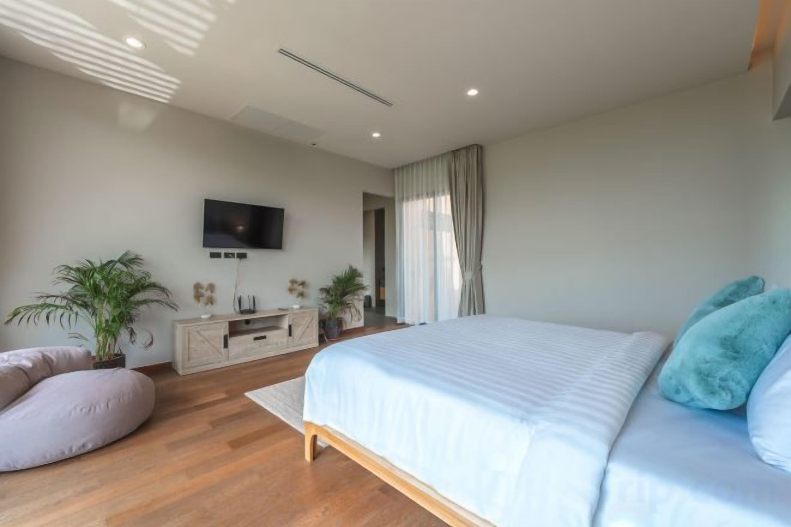 A modern bedroom with a bed, a television, a desk, and a potted plant.