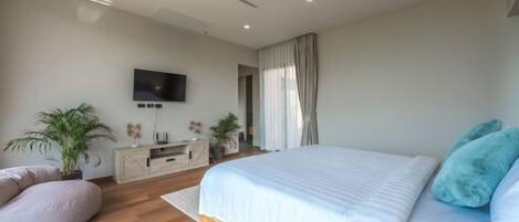 A modern bedroom with a bed, a television, a desk, and a potted plant.
