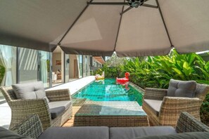 Un espace extérieur avec une piscine, du mobilier en osier et des parasols.