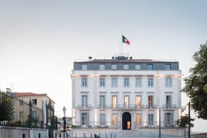 Un grand bâtiment blanc, surmonté d’un drapeau, doté d’un balcon et d’une grande entrée.