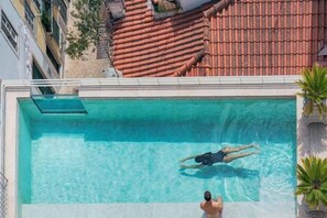 A rectangular swimming pool with clear water, surrounded by a building with red-tiled roofs. - Verride Palácio Santa Catarina (Lisbon)