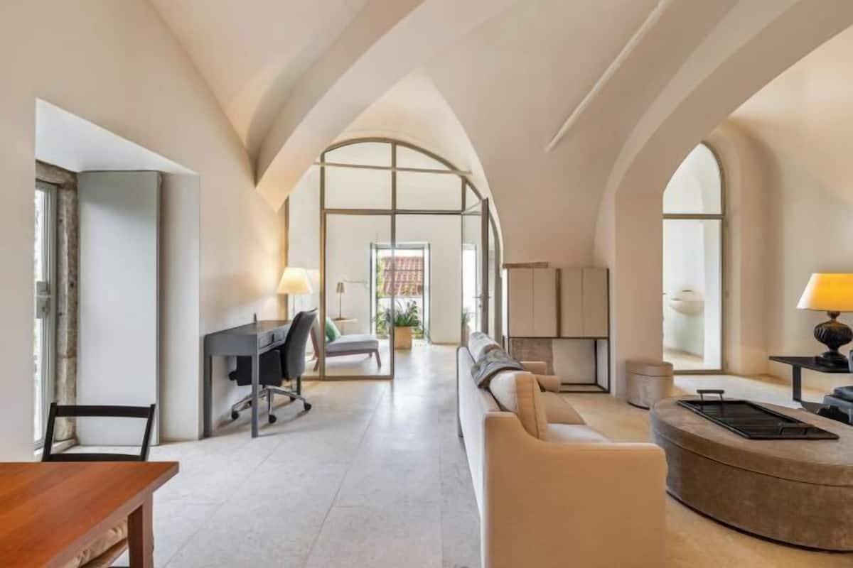 Una habitación amplia con un sofá curvo, un escritorio con una silla y una lámpara.