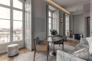 A modern living room with a round table, a sofa, and a large window offering a city view. - Verride Palácio Santa Catarina (Lisbon)