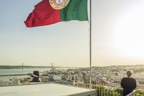 A flag on a flagpole with a cityscape in the background. - Verride Palácio Santa Catarina (Lisbon)