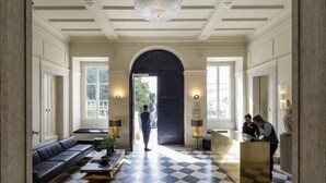 A hotel lobby with a checkered floor, a black sofa, a reception desk, and a large arched doorway. - Verride Palácio Santa Catarina (Lisbon)