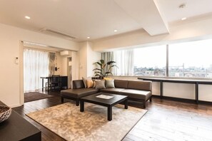 A modern living room with a sofa, coffee table, and a view of the city through large windows. - NC Square Shinjuku -All Suite Residence- (Tokyo)