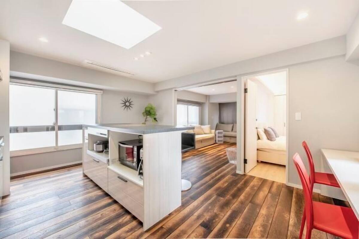 Amplia sala de estar con isla de cocina, comedor con sillas rojas y una zona de estar separada con sofá.