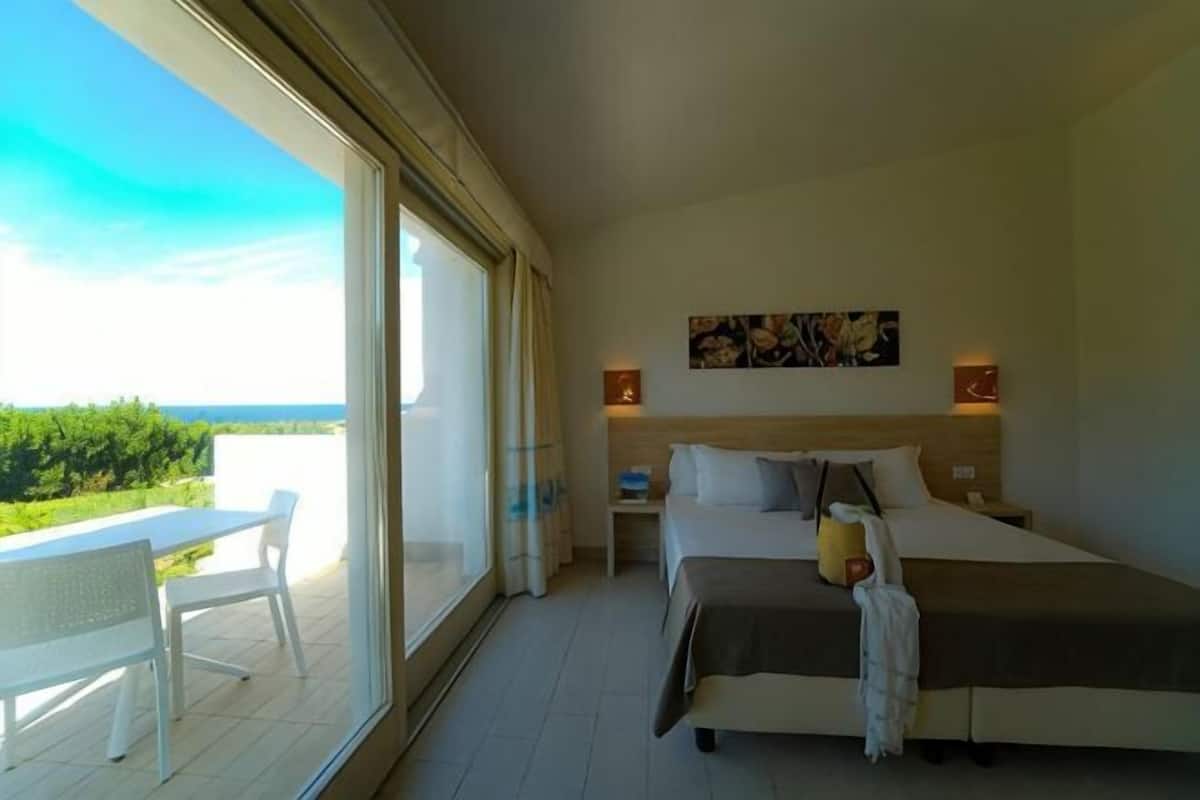 Un dormitorio con cama, mesitas de noche, ventana y vistas a zonas verdes.