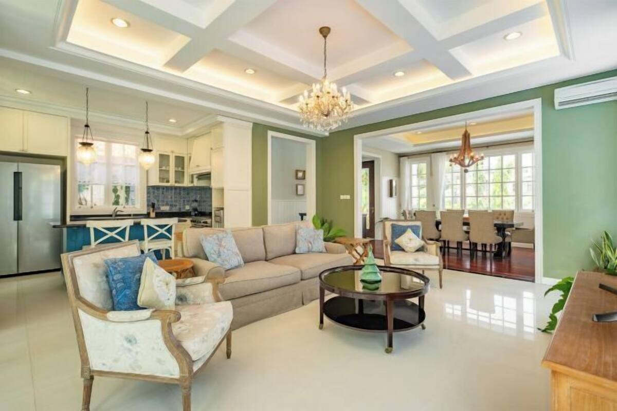 A spacious living room with a large sofa, a coffee table, and a dining area in the background.