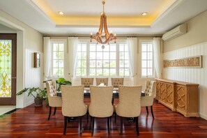 A dining room with a wooden table and six chairs, large windows, and a chandelier. - Viki Nest by SooBali 4BR (Bali)