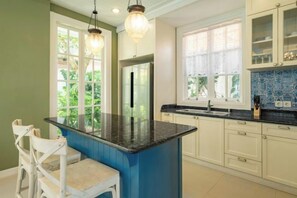 A kitchen with a central island, white cabinetry, and a window with a view of greenery. - Viki Nest by SooBali 4BR (Bali)