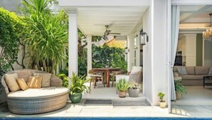 A poolside area with a round wicker sofa, a dining table, and various potted plants. - Viki Nest by SooBali 4BR (Bali)