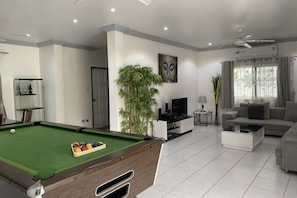 A modern living room with a pool table, a sofa, a TV, and a plant.