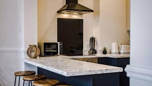 A kitchen with a marble countertop, wooden stools, a black range hood, and a small island with a kettle. - Host & Stay Seel St Townhouse Apt II (Liverpool)