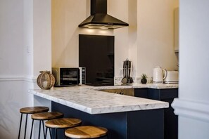 A kitchen with a marble countertop, wooden stools, a black range hood, and a small island with a kettle. - Host & Stay Seel St Townhouse Apt II (Liverpool)