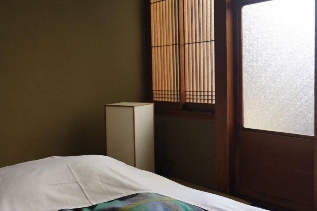 A room with a bed, a cabinet, and a window with bamboo blinds.