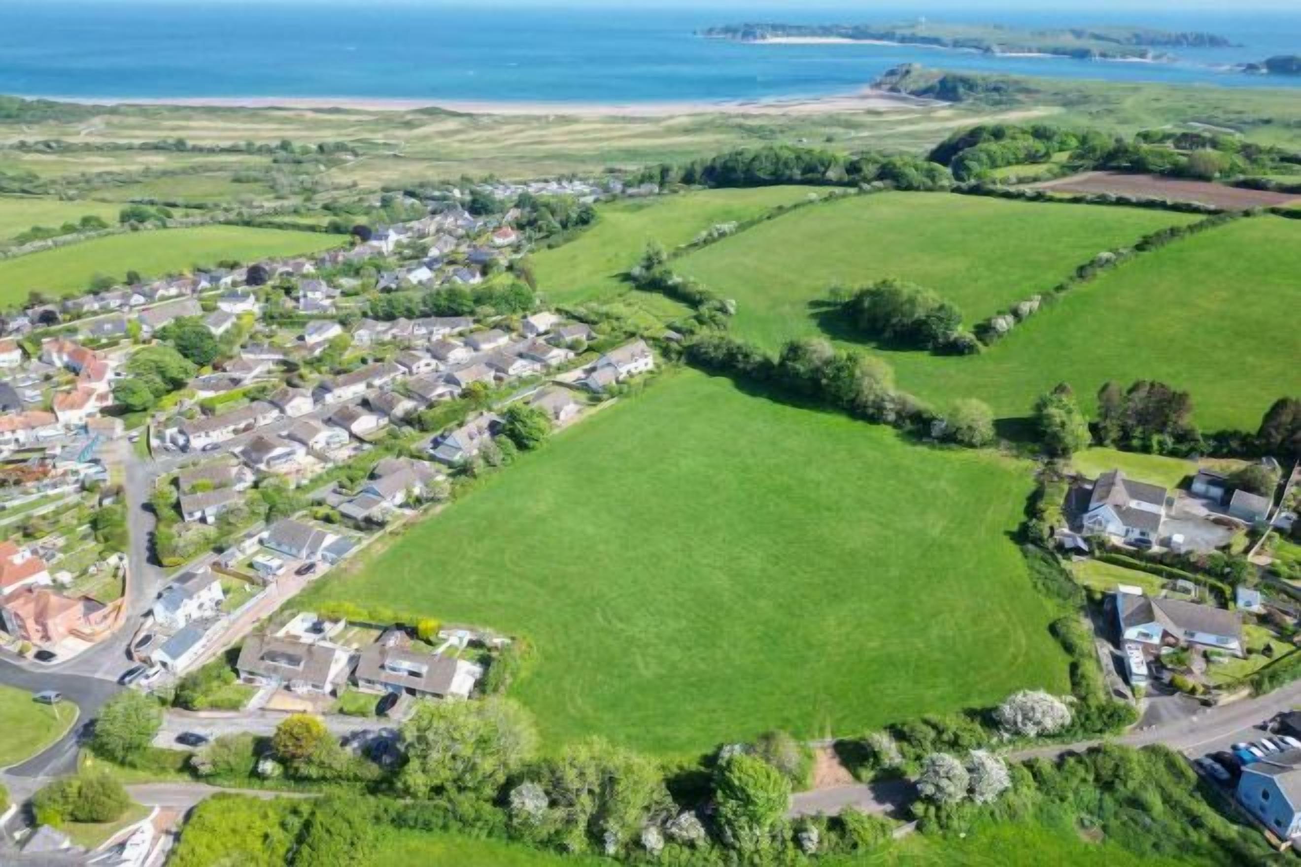 An aerial view of a residential area with houses, roads, and green fields.