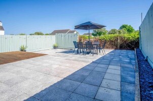 Un patio con una mesa y sillas, una terraza de madera y una sombrilla azul.
