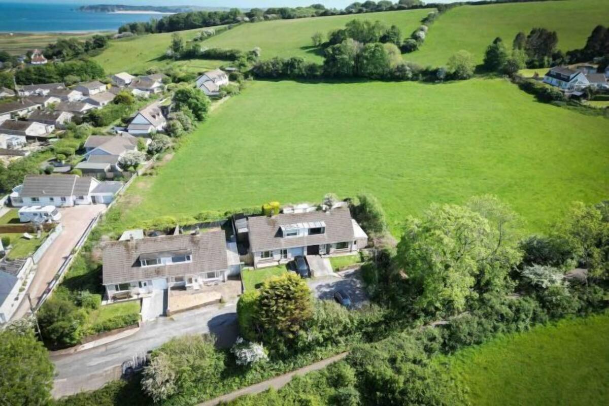An aerial view of a residential area with houses, a large green field, and a body of water in the background.