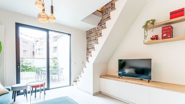 Un salon moderne avec un escalier, un téléviseur et un coin repas comprenant des chaises et une table.