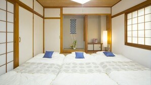 A traditional Japanese-style room with tatami flooring, a low ceiling, and a sliding door. - Guest House Matsuyama (Naha)