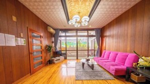 A room with wooden walls, a pink sofa, a glass door, and a chandelier. - Guest House Matsuyama (Naha)