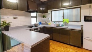 A modern kitchen with dark cabinets, a white countertop, a window with blinds, a microwave, and a refrigerator. - Guest House Matsuyama (Naha)