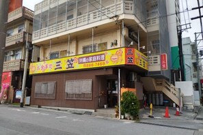 A building with a storefront featuring a sign with Japanese characters and a phone number. - Guest House Matsuyama (Naha)