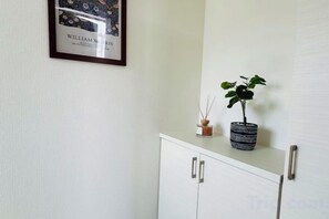 A white cabinet with two doors, a framed picture on the wall, and a potted plant on top. - fukunosou kuukou1goutou (Fukuoka)