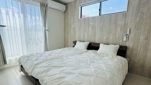 A bedroom with a bed, a window, and a wall-mounted air conditioner. - fukunosou kuukou1goutou (Fukuoka)