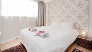 A hotel room with a large bed, two towels, a nightstand, and a patterned wallpaper. - Stylish Apt w/ Charming Balcony in the Very Center (Tel Aviv)