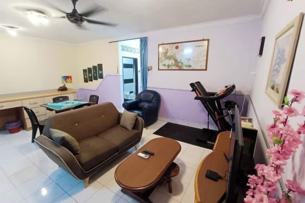 Ein Wohnzimmer mit Sofa, Couchtisch, Fernseher, Heimtrainer und einem Schreibtisch mit Stuhl.