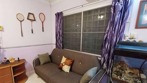 A living room with a sofa, a window with curtains, a fish tank, and wall-mounted badminton rackets. - Kota 3BR Townhouse 5 Pax - TVBox/Mahjong/Jonker (Melaka)
