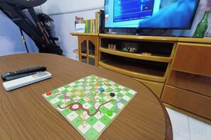 A board game on a table, a remote control, and a television in a room with wooden furniture. - Kota 3BR Townhouse 5 Pax - TVBox/Mahjong/Jonker (Melaka)