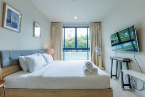 A hotel room with a large bed, a flat-screen TV, a sofa, and a view of a balcony. - Beach Front Condo, Baan Thew Talay Blue Sapphire (Cha-am)
