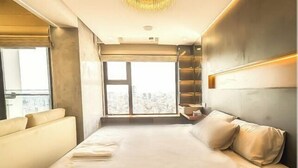 Una habitación de hotel moderna con una cama grande, un sofá, vistas a la ciudad y un estante empotrado.