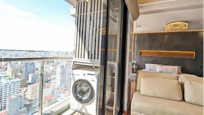 Un apartamento moderno con un ventanal grande, lavadora, sofá y una estantería decorativa.