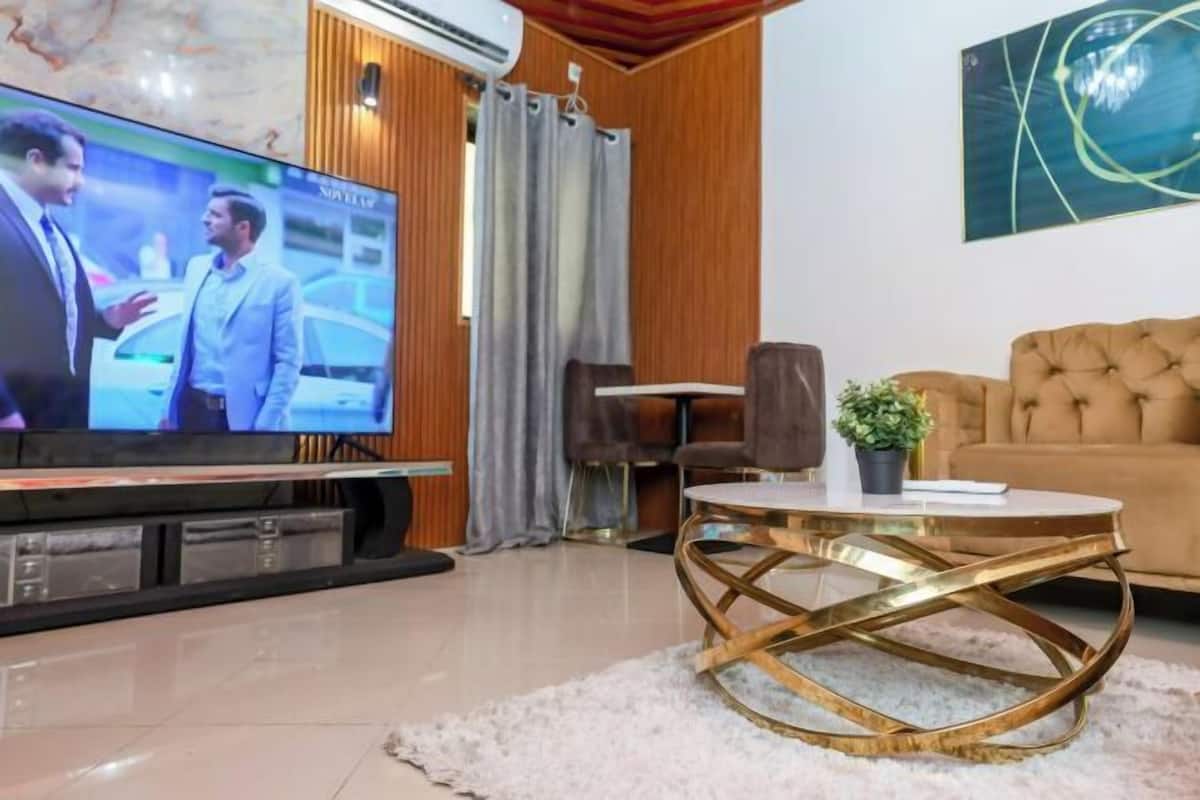 Un salon doté d’un téléviseur à écran plat, d’un canapé capitonné, d’une table basse ronde et d’un mur décoratif en bois.