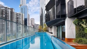 A rooftop pool with a glass barrier, surrounded by high-rise buildings and a clear sky. - A Cozy Apt with City Views Near Crown Casino (Southbank)