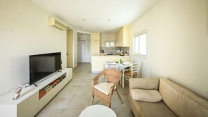 A living room with a TV, a sofa, a dining table with chairs, and a kitchen in the background. - Skyline 1BR Apartment with City and Sea View (Herzliya)