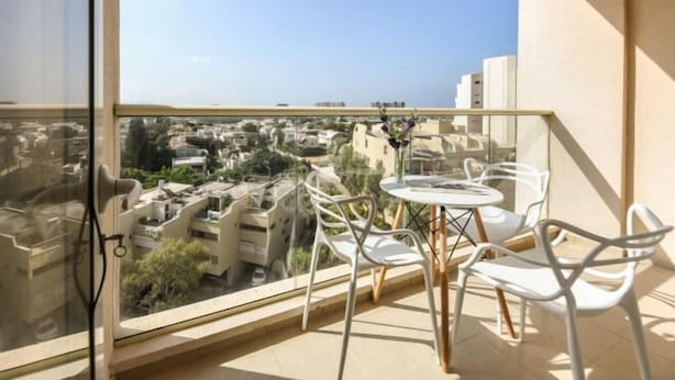 A balcony with a glass door, white chairs, and a small round table. - Skyline 1BR Apartment with City and Sea View (Herzliya)